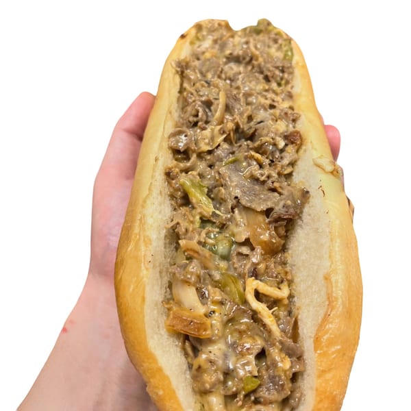 Hand holding a large, open-faced cheesesteak sandwich filled with meat, cheese, and peppers.