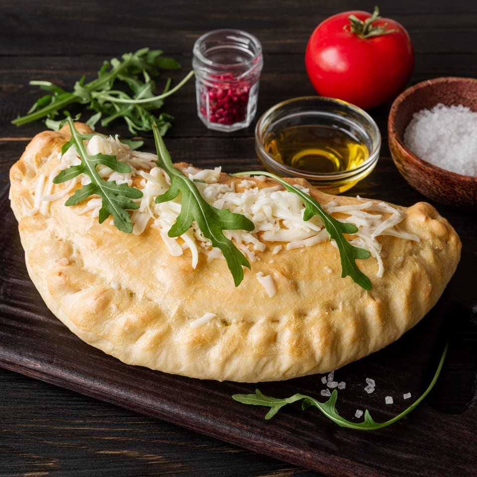 Greco's Pizzeria calzone topped with cheese and arugula, with tomato, oil, and spices.