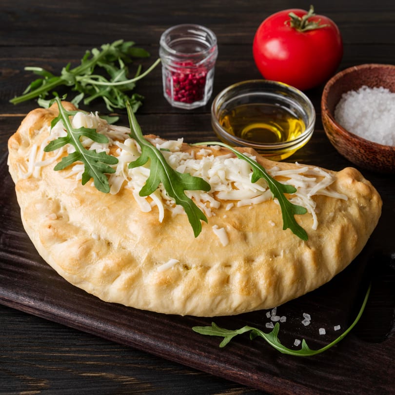 Greco's Pizzeria calzone topped with cheese and arugula, with tomato, oil, and spices.