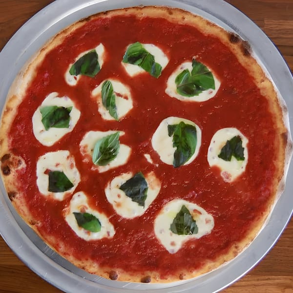 Greco's Pizzeria's Margherita pizza with fresh mozzarella, basil, and rich red sauce on a metal tray.