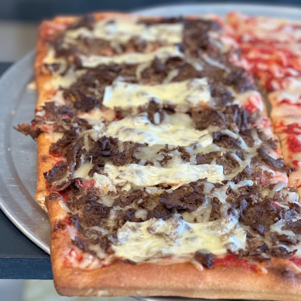 Close-up of a rectangular pizza with steak and cheese, next to a plain cheese pizza.