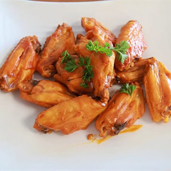 A white plate piled high with golden-brown chicken wings, garnished with fresh green parsley.
