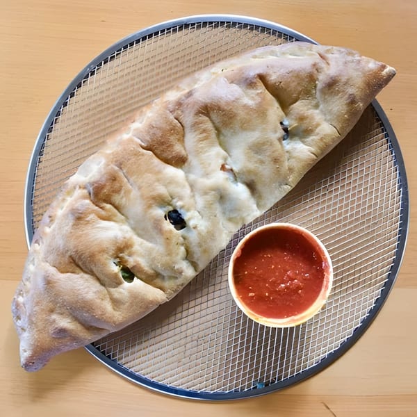 A Greco's Pizzeria calzone with black olives and a side of marinara sauce on a pizza screen.