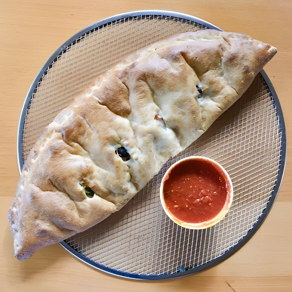 A Greco's Pizzeria calzone with black olives and a side of marinara sauce on a pizza screen.