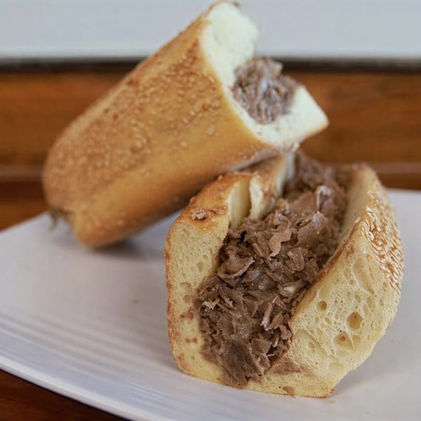 Two halves of a steak sandwich with thinly sliced meat on a white plate.