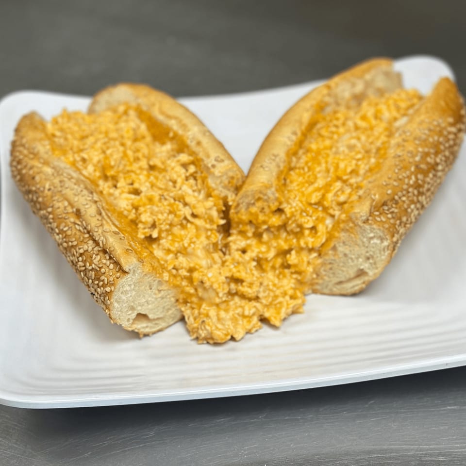 Two halves of a sesame seed sub roll filled with creamy, orange buffalo chicken dip on a white plate.