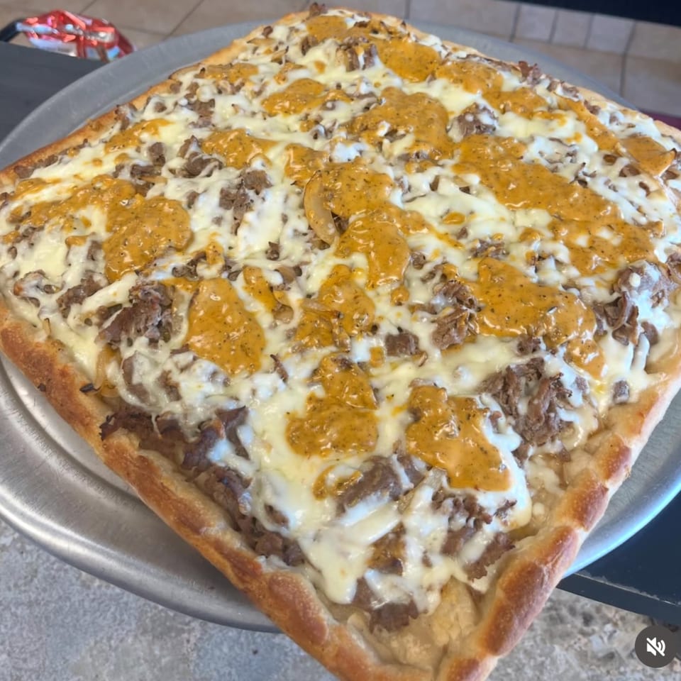 Square pizza with white cheese, ground meat, and a yellow sauce drizzled on top.